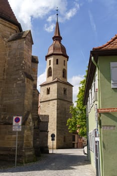 Feuchtwangen, Germany - June 6, 2023: A narrow cobblestone street winds its way between stone buildings and leads to a tall church tower with a pointed spire in a charming German village.