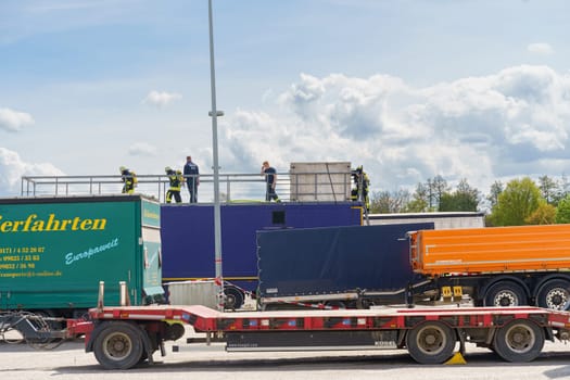 Feuchtwangen, Germany - June 6, 2023: Firefighters practice rescue techniques on a flatbed truck, surrounded by other large trucks in an open area.