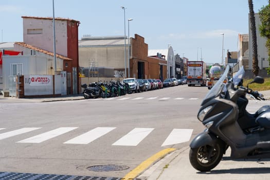 Barcelona, Spain - June 8, 2023: A gray scooter is parked on a street in Spain. The scooter is in front of a crosswalk and there are other vehicles parked on the street.