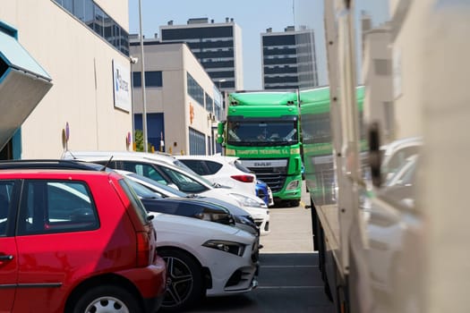 Barcelona, Spain - June 8, 2023: A green semi-truck is parked near a row of several cars in a city parking lot on a sunny day.