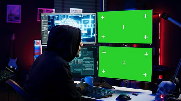 Hacker using AI and green screen computer monitors to produce malicious malware corrupt company data. Evil man working on mockup desktop PC using artificial intelligence, infecting systems, camera B