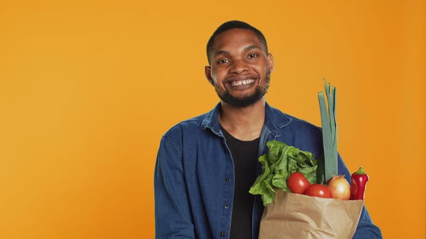 Portrait of cheerful guy pleased with homegrown groceries in a paper bag, feeling happy with his freshly harvested goods to support sustainable lifestyle. Vegan nutrition healthy eating. Camera A.