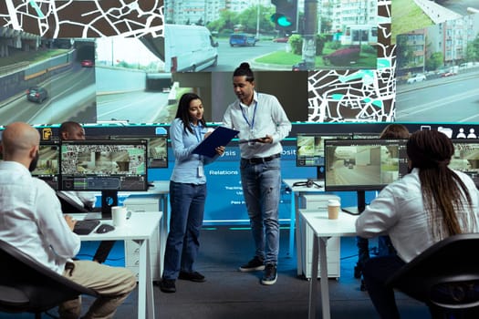 Indian team of operators instructing their colleagues to use CCTV surveillance footage and guide couriers in traffic. Employees operating with global positioning system in satellite map.