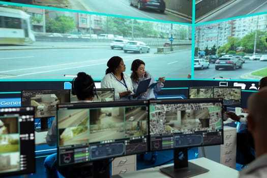 Employees team monitoring urban traffic with radar sensors on a big screen, using real time surveillance footage to ensure public safety. Agency utilizing CCTV satellite system on the streets.