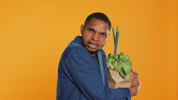 Vegan person acting overprotective of his eco friendly groceries bag, protecting his freshly harvested goods in studio. Serious man taking care of his bio organic belongings. Camera A.