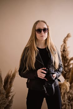 A woman photographer, a blonde with a camera, seriously in the production photo studio. Wearing a black clothes on a brown background