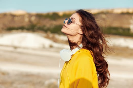 Stylish woman in sunglasses and yellow shirt standing confidently in the desert with head held high