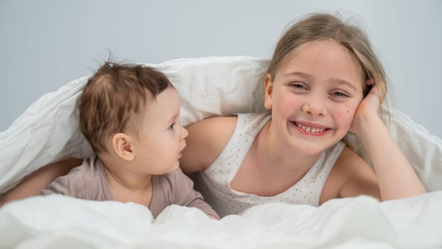 Little girl and her newborn brother hiding under the blanket