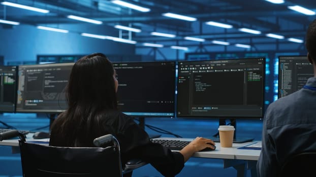 Woman with impairment next to diverse coworkers in data center coding on computer. Wheelchair user and multiethnic team working together, in inclusive and diverse workspace, doing programming