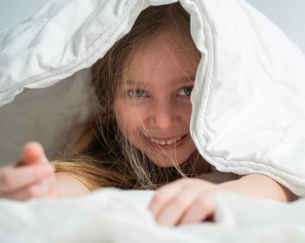 Portrait of a cute little girl laughing and hiding under the blanket