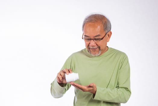 Portrait Asian older man is holding a white pill bottle and spilling in his hand studio shot isolated on white background. He is smiling and he is happy, senior man frug medicine bottle