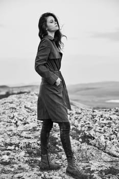 serene woman in trench coat standing on mountain peak overlooking vast ocean vista