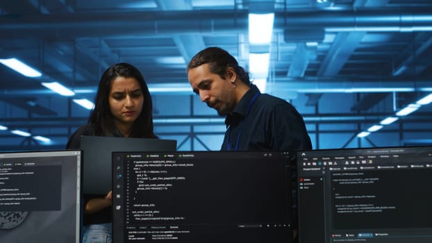 Developer in server hub using laptop to present manager plan of repairing equipment storing datasets. Specialist uses notebook to explain team leader ways of fixing rigs doing computational operations