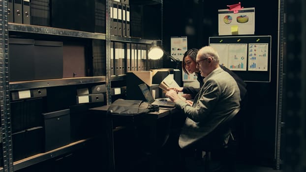 Inspectors team reviewing case information and reading witness statements to create a profile for the suspect. Detectives look into forensic evidence in police archive room, criminology. Camera B.