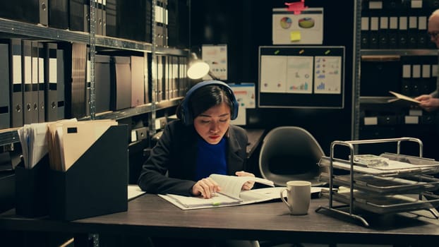 Agent extracting cryptic references found in classified records that may require further deciphering or analysis, archive room work. Law officer trying to break codes to find details. Camera B.