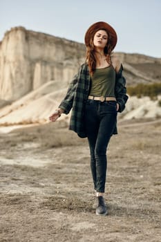 Serene young woman in plaid shirt and hat admires stunning desert landscape with mountains afar