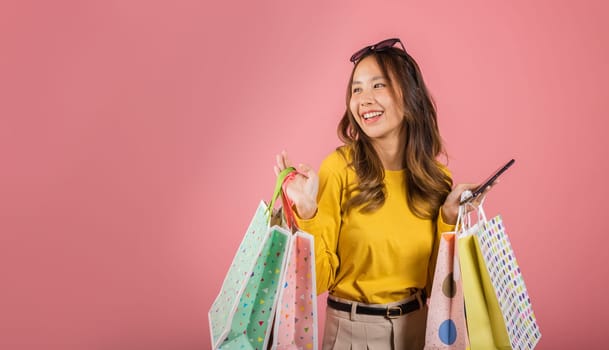 Portrait Asian happy beautiful young woman teen shopper smiling standing excited holding online shopping bags online colorful on mobile phone or smartphone studio shot isolated on pink background