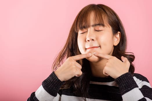 Portrait teenage Asian beautiful young woman having skin problems squeezing pimples acne on her face, studio shot on pink background, with copy space, Thai female acne, beauty care concept