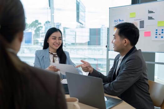 Business team engaged in a strategy discussion with documents and laptops in a modern office setting, highlighting leadership, teamwork, and effective communication