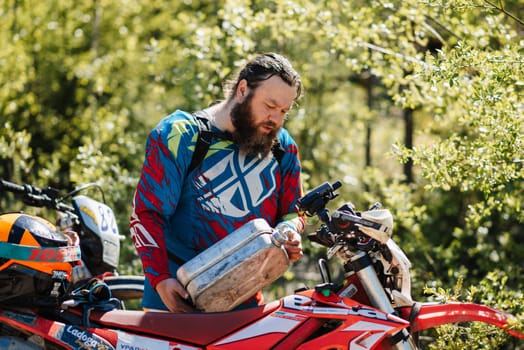 REPUBLIC OF KARELIA, RUSSIA - CIRCA JUNE, 2022: Off-road tournament Ladoga Trophy 2022 in Karelia. A motorcycle racer fills gasoline from a canister into the tank before the start of the race