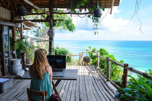 Woman working on laptop at oceanfront table on wooden deck overlooking the sea