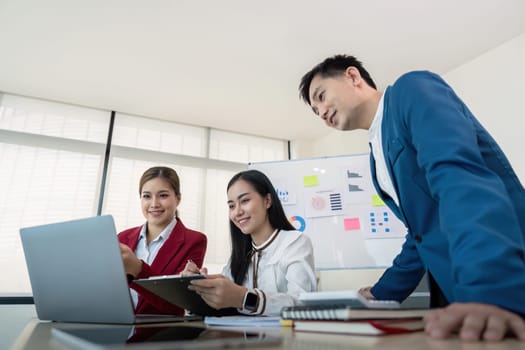 Business team collaborating on a project using a laptop in a modern office setting, showcasing teamwork and productivity