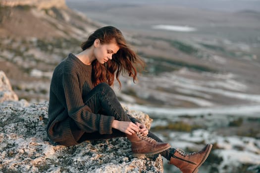 Woman sitting on mountain peak, gazing at valley below with boots on