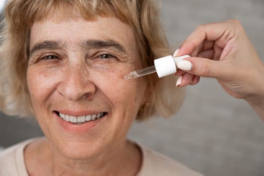 Close-up portrait of an old woman applying hyaluronic acid serum with a pipette. Anti-aging face care