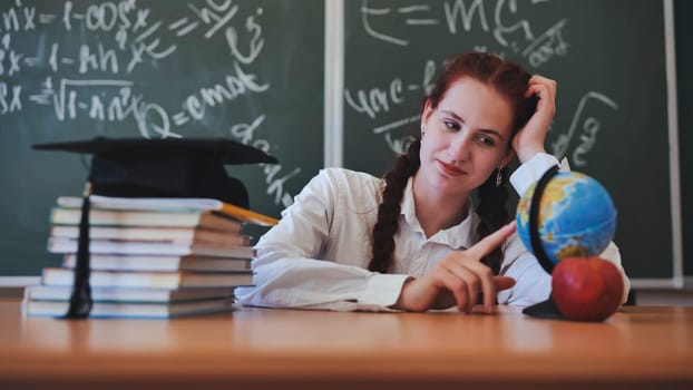 A red-haired high school senior poses against a backdrop of books, a globe and a graduation cap