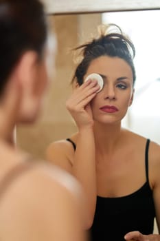 Beautiful young brunette woman washes away makeup in front of bathroom mirror