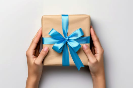 A person is holding a gift with a blue ribbon on it. The gift is wrapped in brown paper and has a bow on top