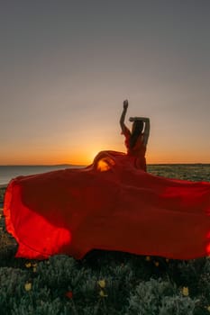 A woman in a red dress is standing in a field with the sun setting behind her. She is reaching up with her arms outstretched, as if she is trying to catch the sun. The scene is serene and peaceful