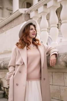 A woman in a hat stands on a set of stairs in front of a building. She is wearing a coat and a skirt