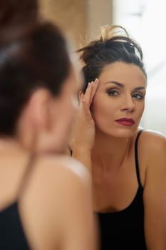 Beautiful young woman brunette watching face closely in front of bathroom mirror