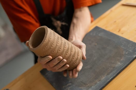 Close-up of a man's hands making a patterned cylinder out of clay