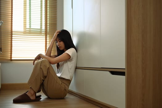 Unhappy young woman thinking about problems sitting on floor at home. Mental problems concept.