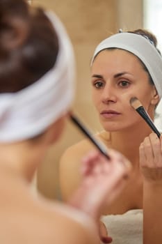 Beautiful young brunette woman applying fluid in front of bathroom mirror