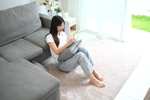 Smiling young woman freelancer in casual clothes using digital tablet at home.