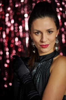 Beautiful young brunette woman poses in party dress on black shiny background