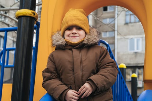 child kid boy playing on a slide on the playground in winter in the park