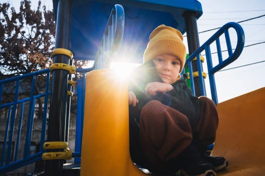 child kid boy play on the playground on the slide in autumn on a sunny day