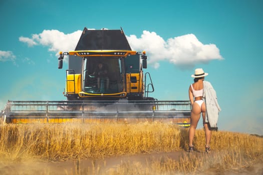 girl stands on a field against the backdrop of a combine harvester,