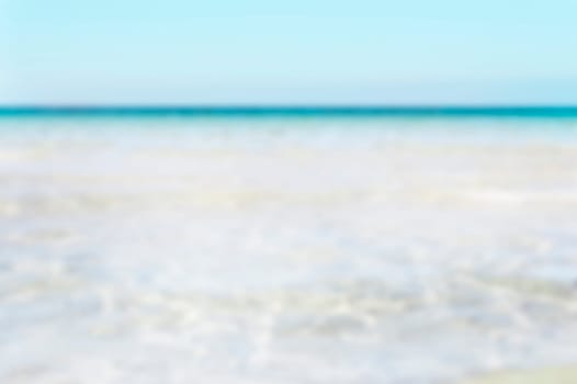 Bumpy tropical sandy beach with blurry transparent ocean and blue sky.