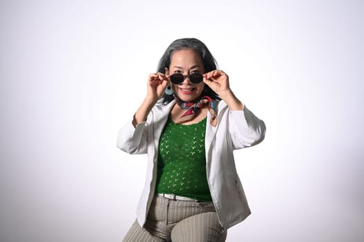 Portrait of fashionable middle age woman wearing sunglasses posing to the camera on white background.