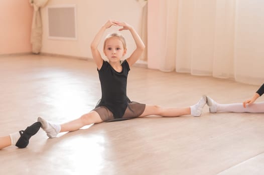 Little girls sit in a circle and do stretching at a ballet school