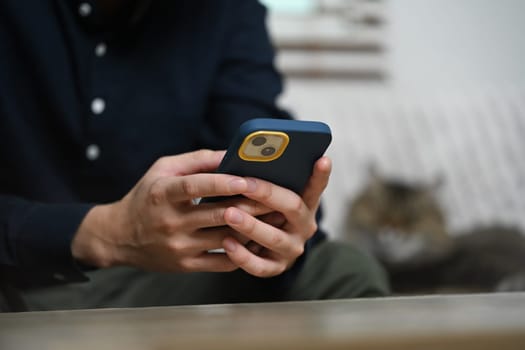 Young man sitting on couch reading text message and chatting in mobile application.