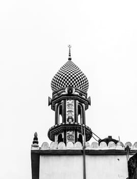 A black and white photo of a mosque in India, showing a close up of the checkered dome with a crescent moon on top. The photo is taken from a low angle, looking up at the dome. The mosque is a beautiful example of Islamic architecture, and the checkerboard pattern of the dome is a unique and interesting design element.