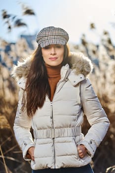 Beautiful young brunette woman in jacket poses on meadow on sunny day