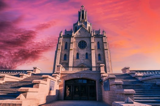 facade of gothic old ancient Catholic Cathedral on background of dramatic cloudy purple sky at sunset. Church of the Sacred Heart of Jesus in Tashkent in Uzbekistan