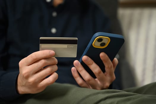 Man holding credit card making payment on mobile phone. Internet banking and shopping online concept.